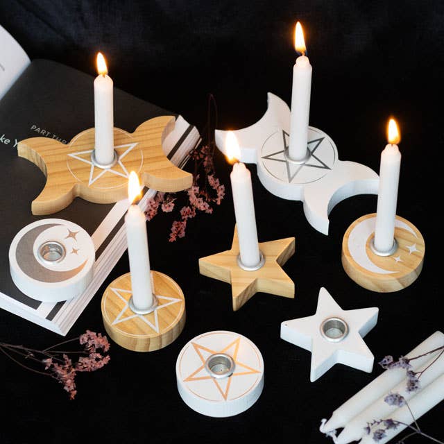 Spell candle holders with pentagram middle and moons with lit candles on a dark surface.