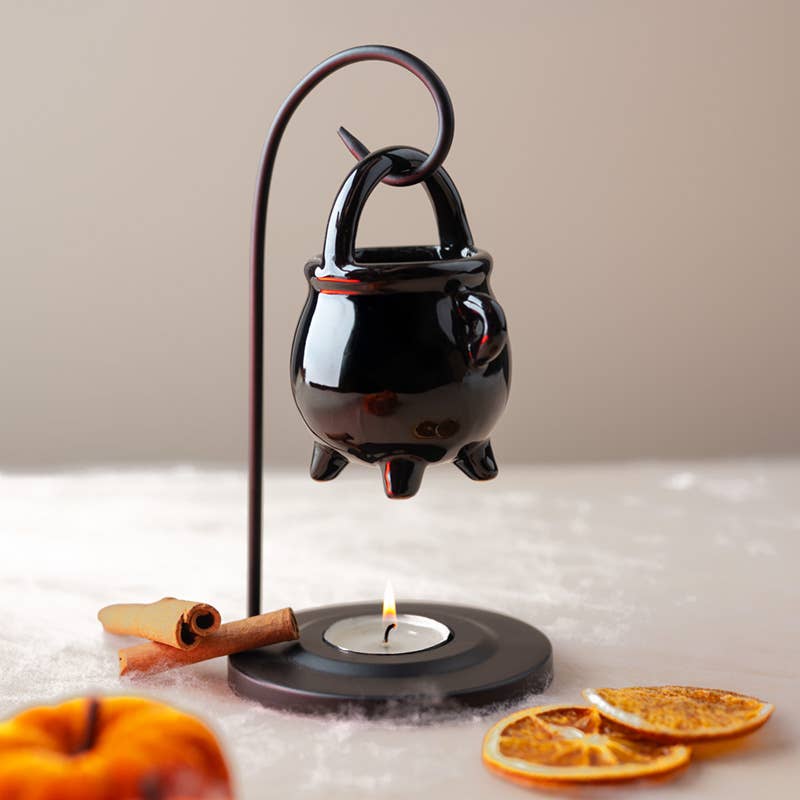 Black ceramic cauldron with a candle on a white surface with orange slices and a cinnamon stick.