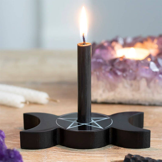 Black spell candle holder with a lit candle on a wooden surface with purple crystals in the background.