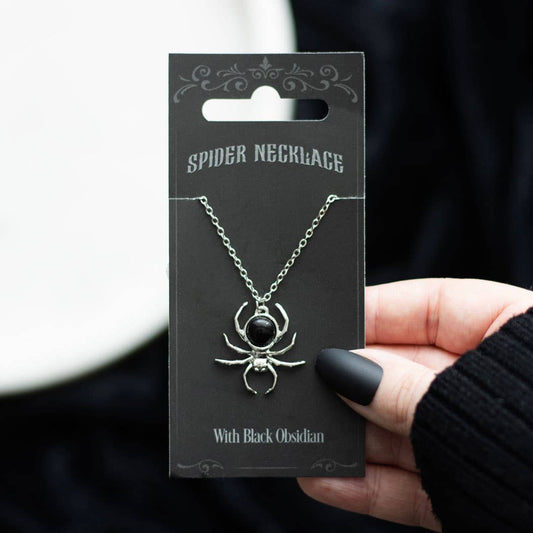 Spider necklace with black obsidian on a black card held by a hand.